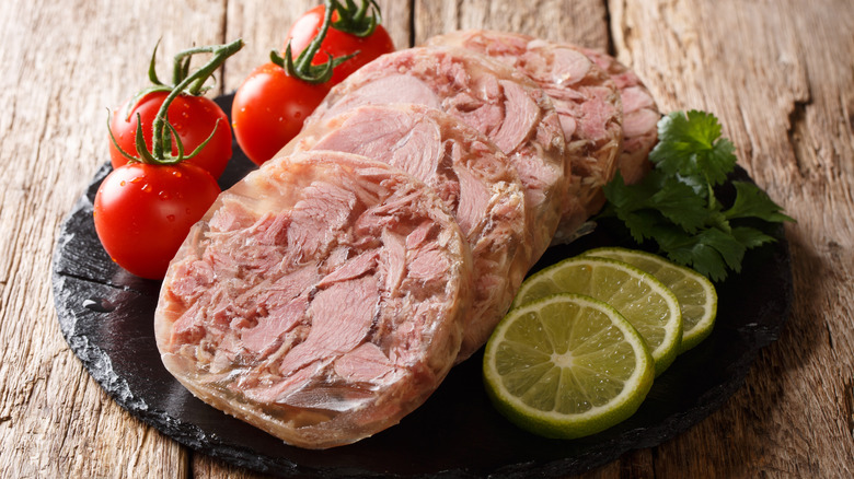 Sliced head cheese on slate with tomatoes and limes