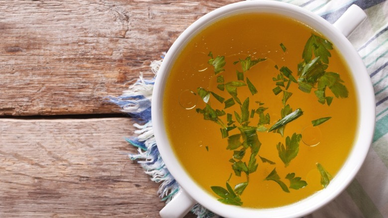 A cup of beef broth with parsley.