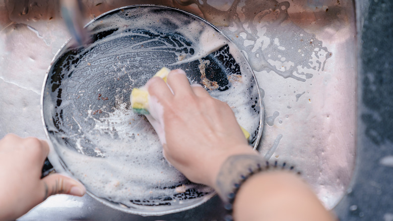 scrubbing a frying pan with soapy water and sponge