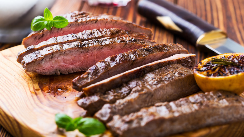 Cut steak on a wooden board, garnished with basil and lemon