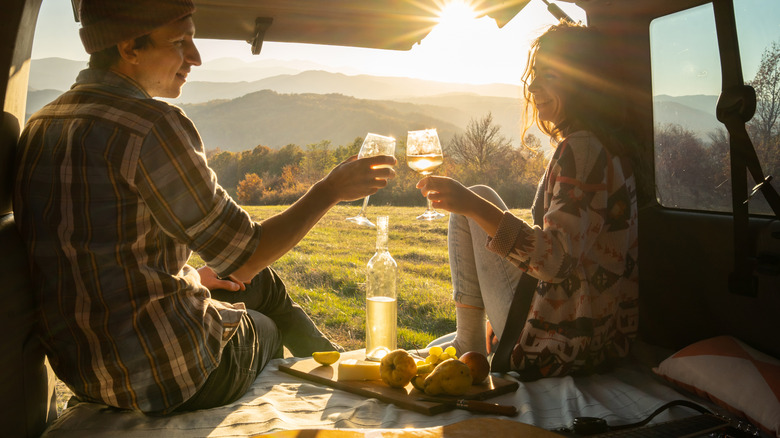 A couple drinks wine in the back of their vehicle on a sunny day