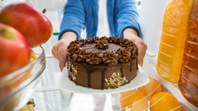 A chocolate frosted cake being placed in the fridge