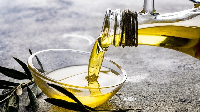 A closeup of a bottle of olive oil being poured into a clear glass dish