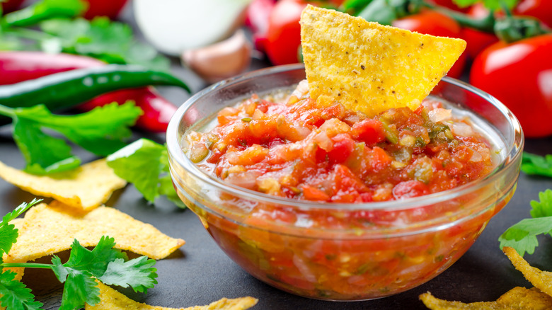 A glass dish of salsa with a tortilla chip in it.