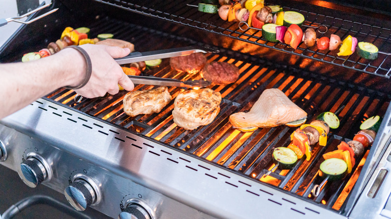 Meat, salmon, and vegetable skewers being cooked on a grill