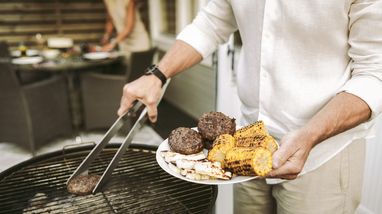 Someone grilling burgers and corn on a charcoal grill