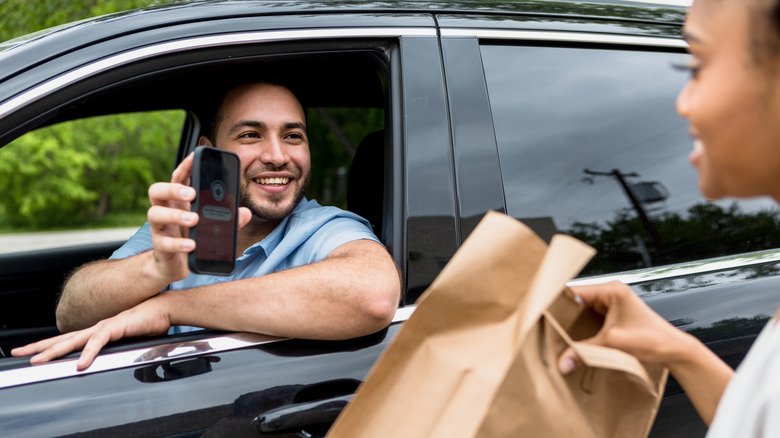 An employee handing over a bag to a curbside customer in a car.