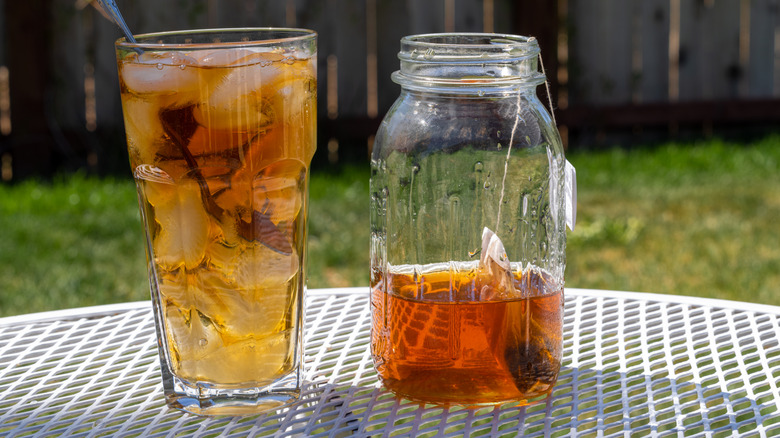 A jar of sun tea and a glass of iced tea on an outdoor table
