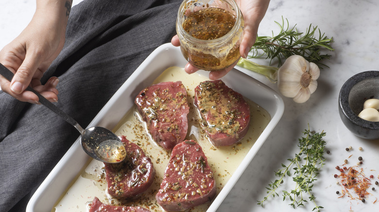 A person coating slabs of steak in a white dish in marinade