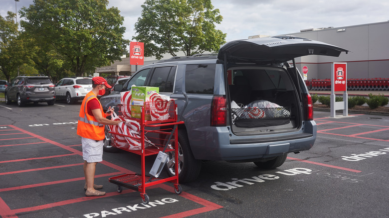 A person in a face mask and orange safety vest retrieves Target bags from a shopping cart next to a car with an open hatchback
