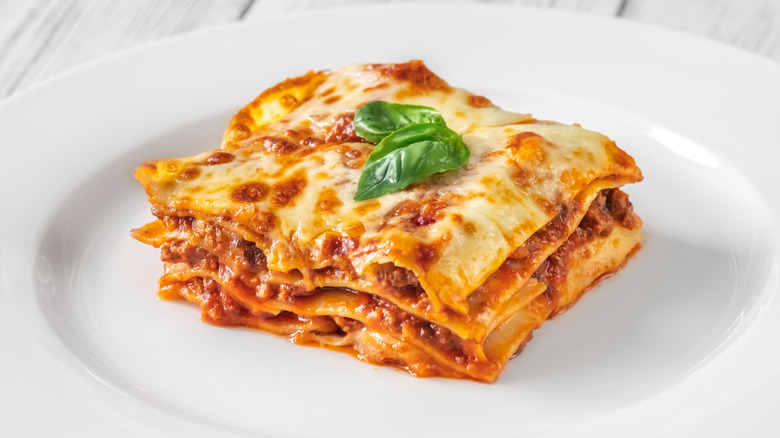 A piece of lasagna on a white plate with two basil leaves on top