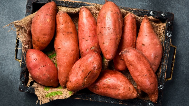 Basket of raw sweet potatoes on a black slate surface.