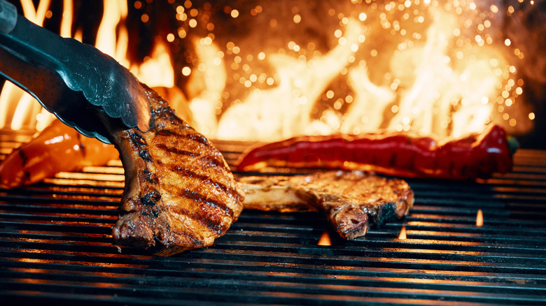 Tongs picking up a pork chop from a fiery grill