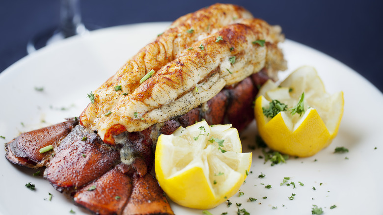 A cooked lobster tail served on a plate with lemons.