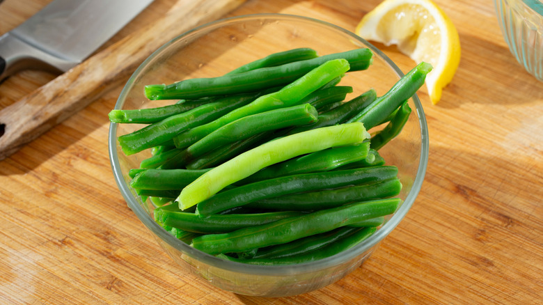 Cooked green beans in a glass bowl on wooden board