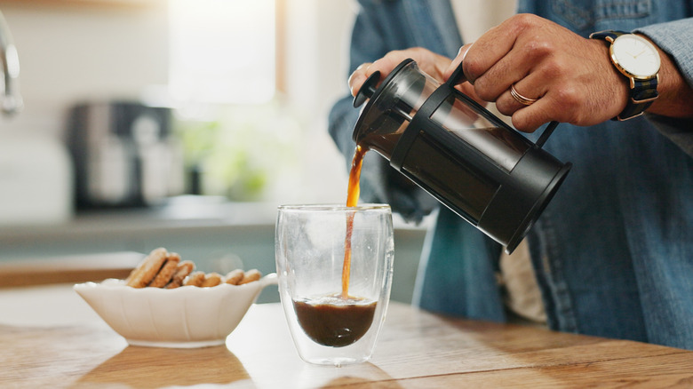 Hands pouring French press coffee into cup