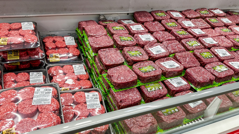 Packages of ground beef and hamburger patties in a grocery store refrigerated case.