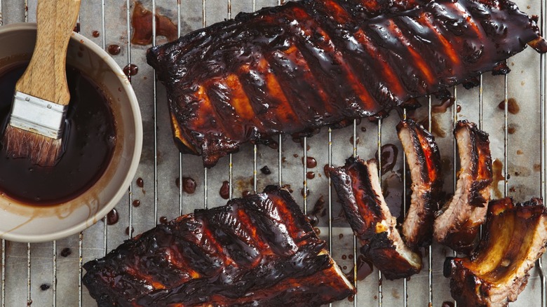 Racks of ribs on a wire rack with a bowl of barbecue sauce