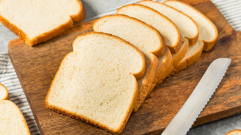 Slices of white bread on a wooden board with a knife
