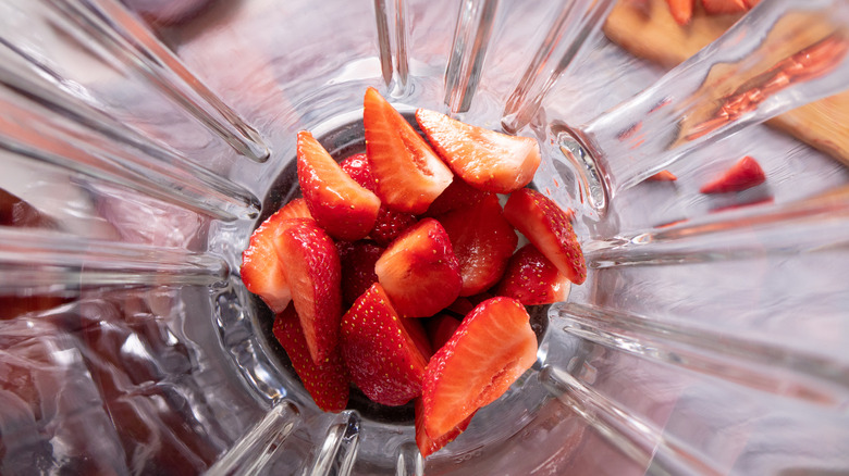 Cut strawberries sitting in a blender, closeup from above