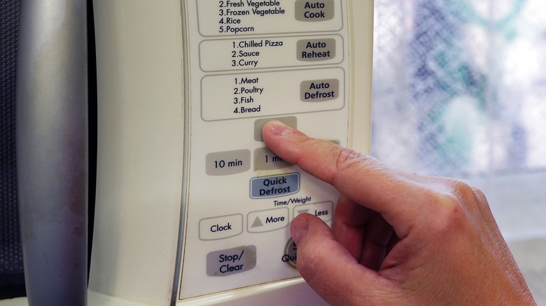 A person pushes a button on the microwave in the kitchen