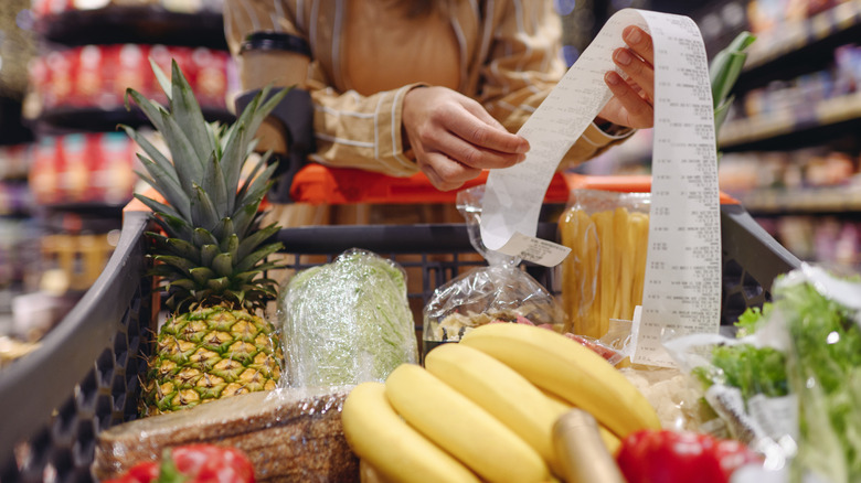 A woman inspects a grocery receipt over a full cart