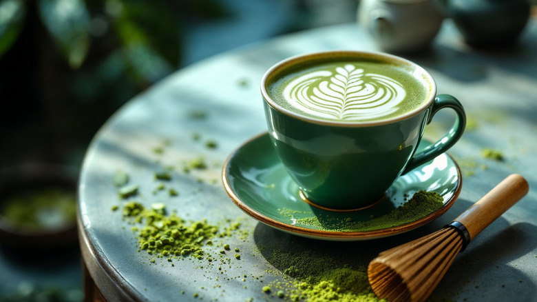 Matcha latte alongside matcha powder and whisk