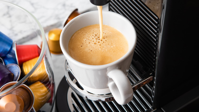 Coffee pours into a mug next to a bowl of coffee pods