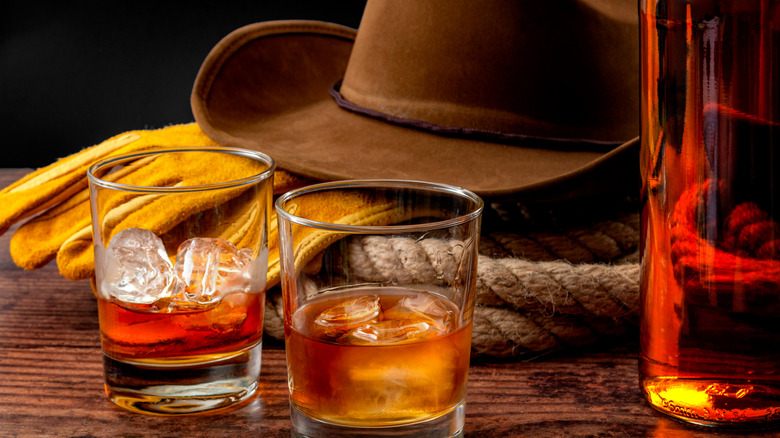 A cowboy hat, gloves, and lasso with two glasses of whiskey on a table.