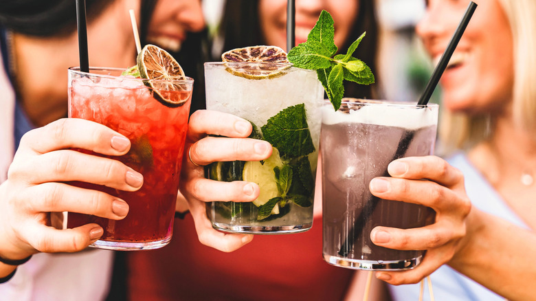 Three women holding different cocktails together as they smile and laugh.
