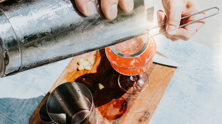 Hands pouring a drink through a strainer from a cocktail shaker