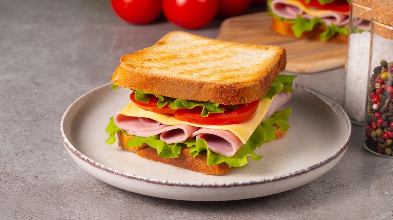 sandwich with ham, cheese, lettuce, and tomato on a white plate