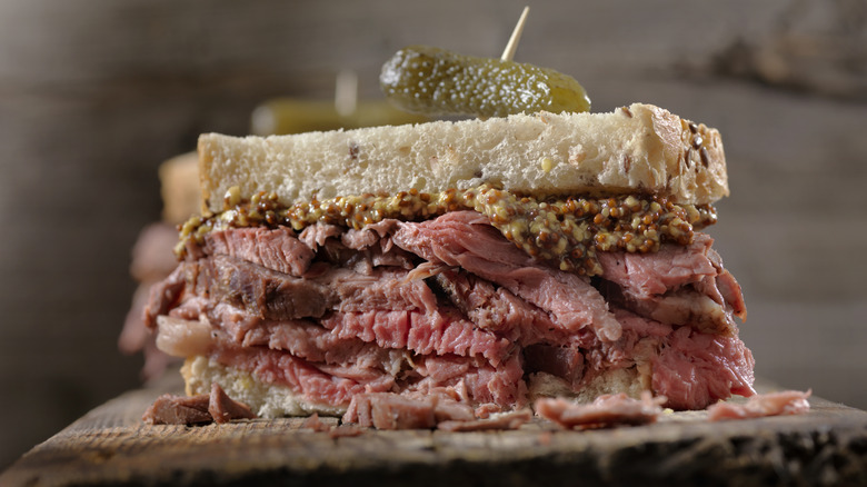 roast beef sandwich with mustard and al pickle on a wooden plank