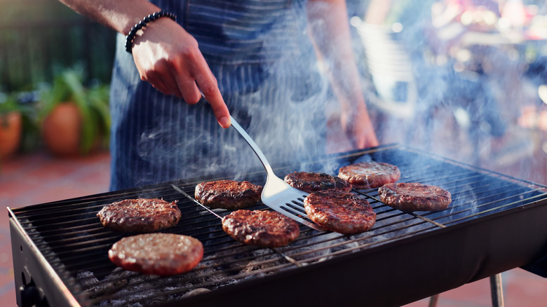 man flipping burger patties on outdoor grill