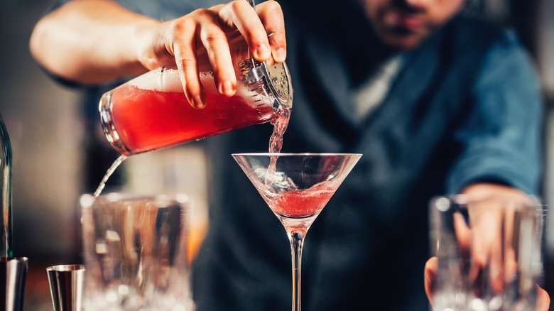 A bartender pouring a red cocktail into a martini glass