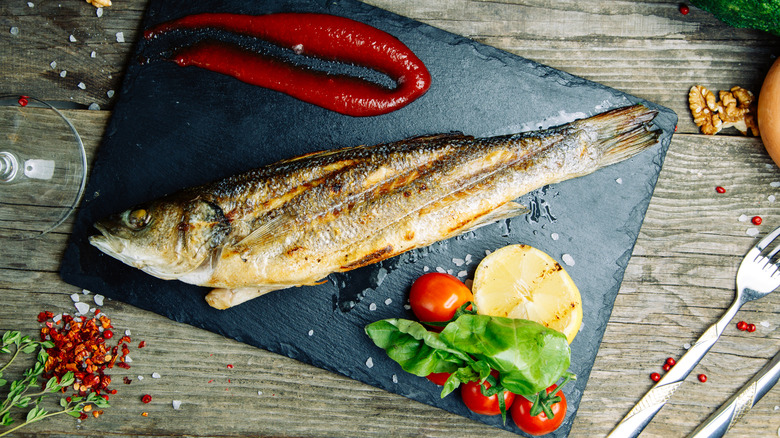 cooked branzino on a black board with a decorative smear of ketchup