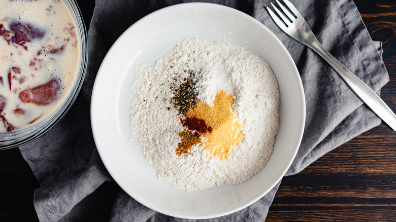 Flour with seasonings and bowl of buttermilk marinated raw chicken