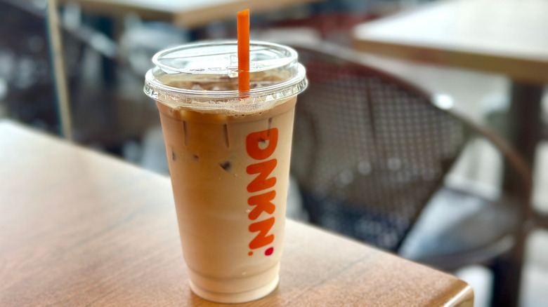 An iced latte from Dunkin' in a plastic cup on a wooden table.