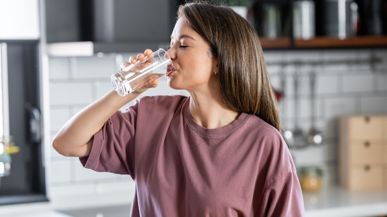 Person smiling while drinking a glass of water in kitchen