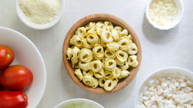 raw tortellini in a bowl surrounded by bowls of other cooking ingredients