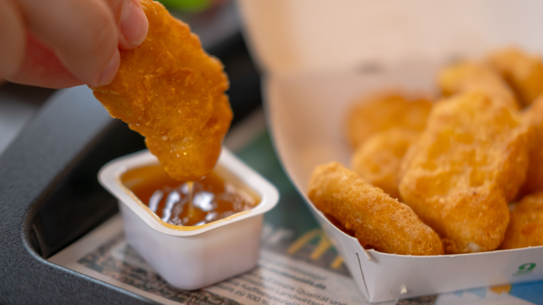 A hand dunks a chicken nugget in sauce with a carton of nuggets nearby