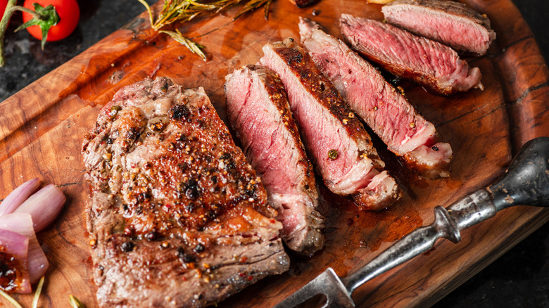 Medium-rare ribeye steak with herbs on a wooden tray