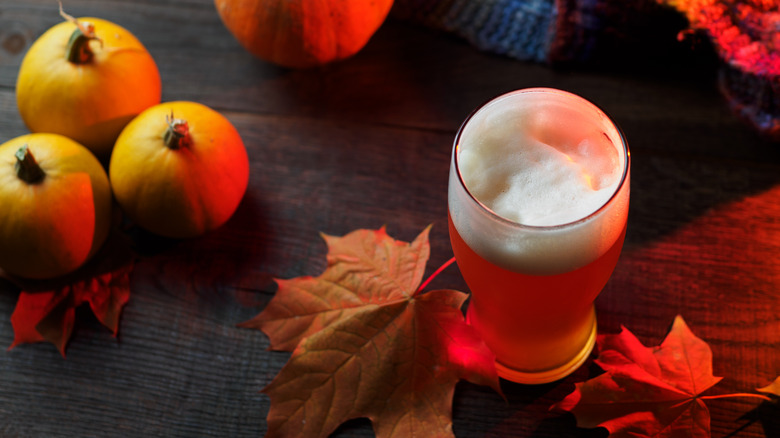 A glass of pumpkin ale with decorative autumn leaves and pumpkins
