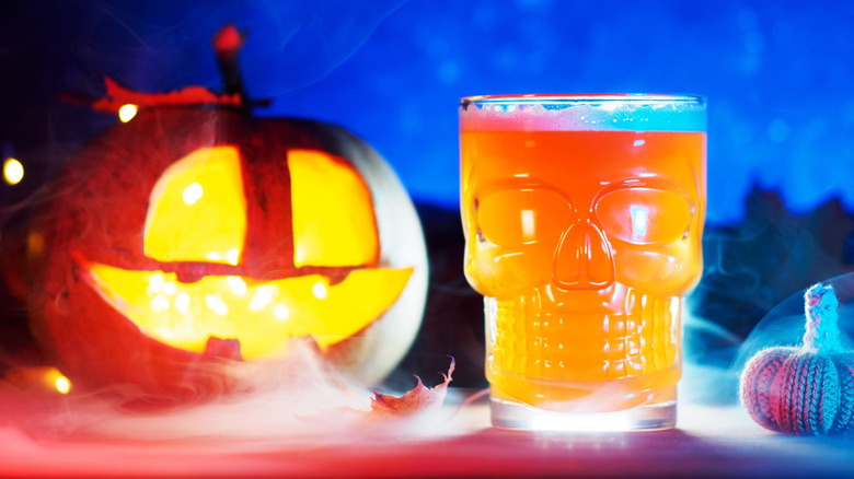 A skull-shaped glass of pumpkin beer with a jack-o-lantern