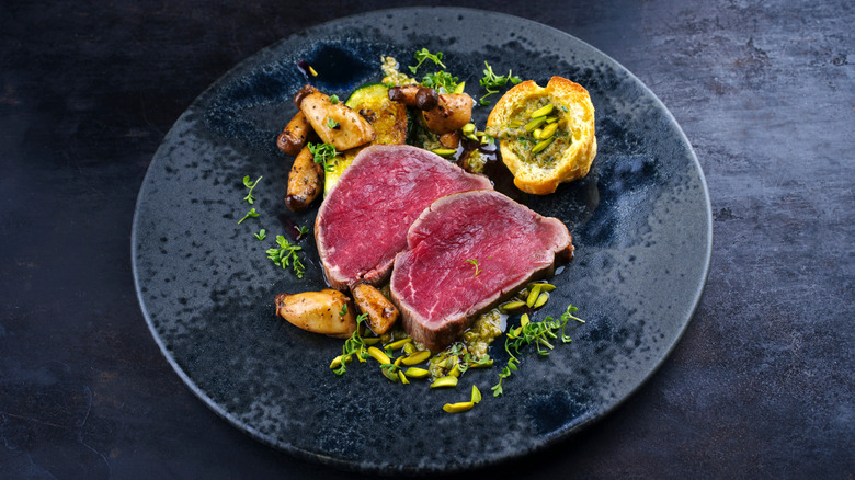 Very rare steak on a plate with roasted potatoes and herbs