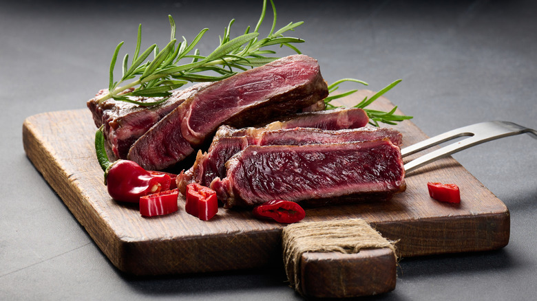 Slices of very rare beef on a cutting board with cut red pepper slices and rosemary sprigs
