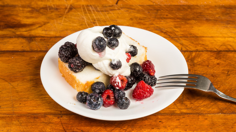 White plate with pound cake slice, berries, and whipped cream