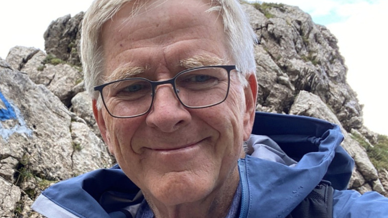 Rick Steves smiles in a blue jacket on an outdoor hike