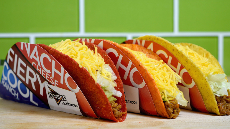 Three Doritos Locos Tacos lined up on a counter with a green tiled background