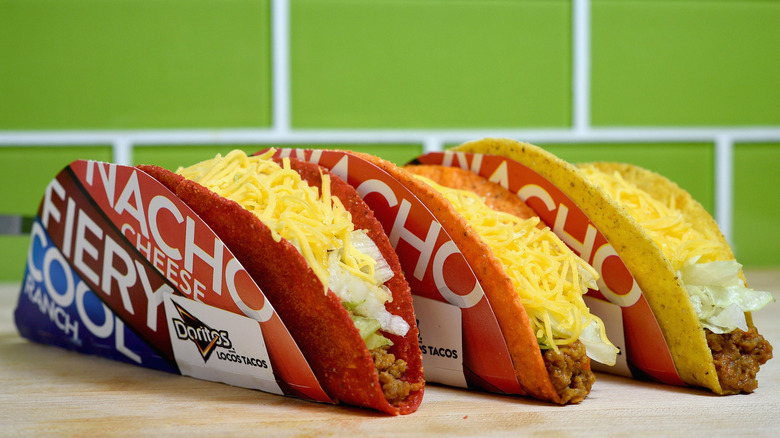 Three Doritos Locos Tacos lined up on a counter with a green tiled background